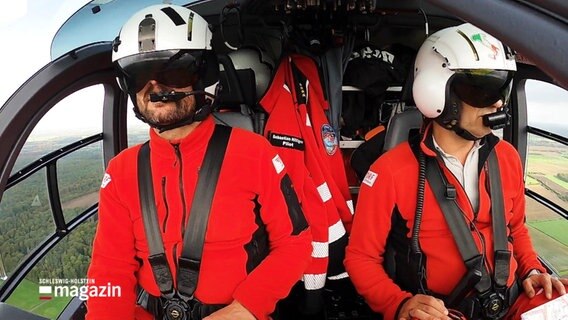 Pilot und Co-Pilot in roter Arbeitskleidung und Helmen in einem Hubschrauber. © Screenshot 