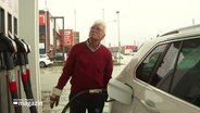 Ein älterer Mann beim Tanken seines Autos; er schaut kritisch auf die Anzeige der Zapfsäule. © Screenshot 