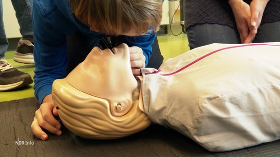 Beim Erste-Hilfe-Kurs: Eine junge Person hat den Kopf über eine Puppe gebeugt um zu spüren, ob der "Patient" atmet. © Screenshot 