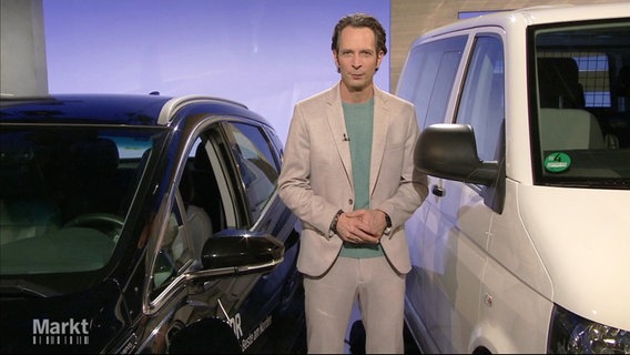 Moderator Jo Hiller steht zwischen einem schwarzen und einem weißen Auto im Studio von "Markt". © Screenshot 