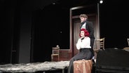 Eine Szene der Komödie "Fisch zu viert", in der eine rothaarige Frau auf einem Stuhl sitzt und ein Mann hinter ihr steht. © Screenshot 