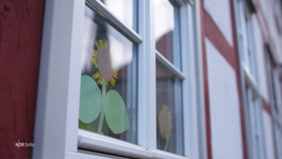 Aus Pappe gebastelte Sonnenblumen hängen in einem Fenster. © Screenshot 