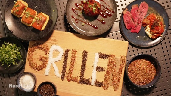 Verschiedene Gerichte auf Tellern, in der Mitte steht das Wort "Grillen" mit Gewürzen geschrieben. © Screenshot 