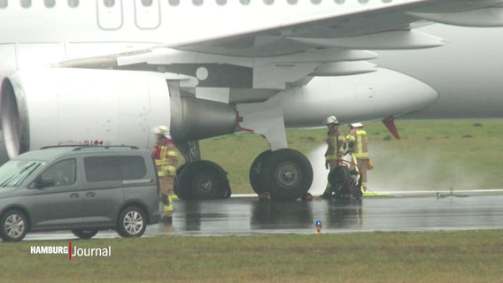 Feuerwehrleute untersuchen den geplatzten Reifen eines Flugzeugs auf einer Rollbahn. © Screenshot 