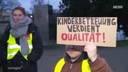 Eine Streikende hält ein Schild mit der Aufschrift "Kinderbetreuung verdient Qualität". © Screenshot 