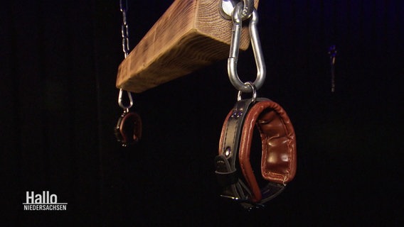 Von der Decke hängt ein Holzbalken mit daran befestigten Lederschnallen zum Fesseln. © Screenshot 