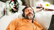 Ein Mann liegt auf dem Sofa und hört ein True-Crime-Podcast. (extra 3 vom 29.02.2024 im Ersten) © NDR 