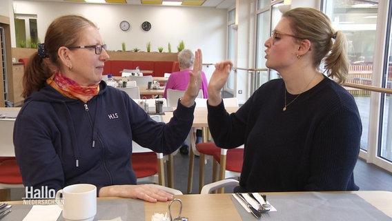 Zwei Frauen sitzen sich gegenüber und kommunizieren über ihre Hände © Screenshot 