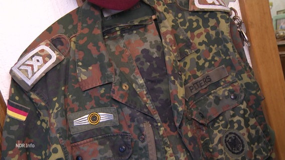 Im Flur einer Wohnung hägt eine Camouflage-Uniform des Reservisten Peters. © Screenshot 