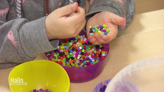 Kleine Kinderhände sortieren bunte Bügelperlen in eine Plastikschale. © Screenshot 