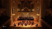 Ein Orchester aus den oberen Rängen eines Theaters gezeigt. © Screenshot 