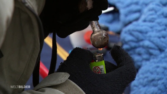 Eine Person erhitzt Drogen in einer Pfeiffe mit einem Feuerzeug. © Screenshot 