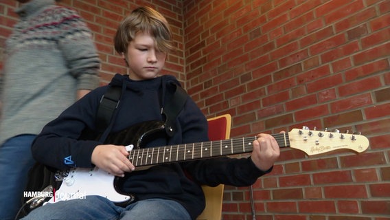 Ein Junge spielt auf einer E-Gitarre. © Screenshot 