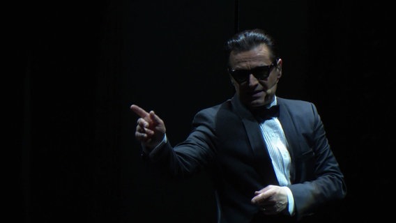 Ein Musical-Darsteller, der wie Falco aussieht auf einer Bühne. © Screenshot 