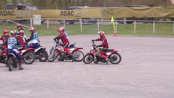 Motorrad-Fahrer in roten und blauen Tricots spielen Motoball. © Screenshot 