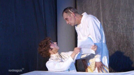 Szene aus einer Inszenierung des Films Nosferatu: Zwei Männer in weiß, der rechte beugt sich bedrohlich über den linken. © Screenshot 