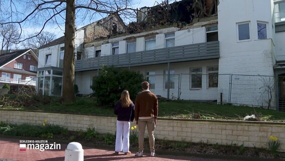 Zwei Jugendliche betrachten ein Haus mit verbranntem Dach. © Screenshot 