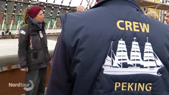 Ein Mann trägt eine dunkelblaue Crew-Jacke der Peking. © Screenshot 