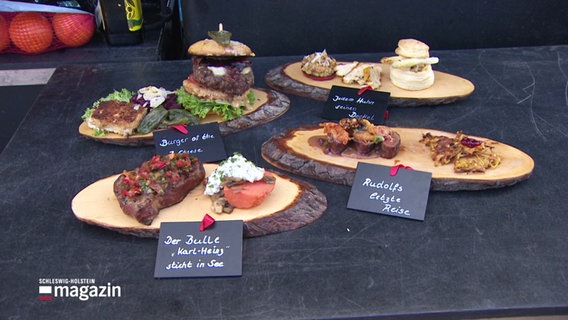 Auf dünnen Kolzplatten sind verschiedene Gerichte vom Grill angerichtet. © Screenshot 