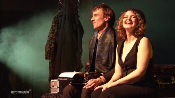 Ein Darsteller und eine Darstellerin des Musicals "Cabaret" im Mecklenburgischen Staatstheater singen sitzend auf der Bühne. © Screenshot 