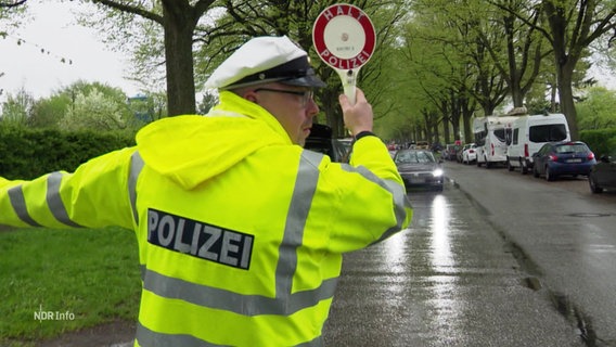 Ein Polizist in Warnweste signalisiert mit einer Kelle Autos zum Anhalten. © Screenshot 