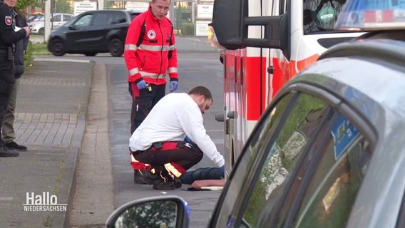 Rettungssanitäter versorgen den am Boden liegenden Radfahrer an der Unfallstelle. © Screenshot 