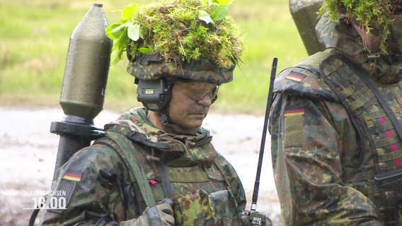 Soldaten in Tarn- und Schutzkleidung sowie mit Moos und Zweigen getarnten Helmen. © Screenshot 
