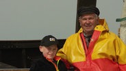 Fischer Uwe Krüger aus Heringsdorf steht in Ölzeug gekleidet neben seinem Enkel Mika. © Screenshot 
