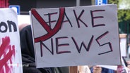 Auf einer Demo wird ein Schild mit der Aufschrift: "Fake News" hoch gehalten. © Screenshot 