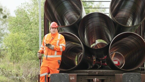 Ein Mann steht auf einem Bahnwaggon der mit Pipeline-Röhren beladen ist. © Screenshot 