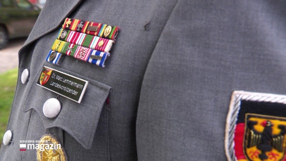 An einer grauen Uniform sind viele Abzeichen befestigt. © Screenshot 