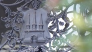Das metallene Wappen Altonas zeigt eine Burg mit offenen Toren. © Screenshot 