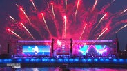 Am Hamburger Hafen leuchtet rotes Feuerwerk hinter einer Bühne auf. © Screenshot 