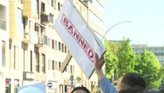Schilder mit der Aufschrift "Banned" werden bei einer Versammlung von Islamisten in die Luft gehalten. © Screenshot 
