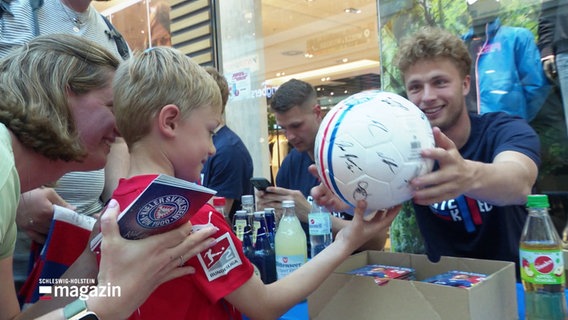 Ein kleiner Junge freut sich über den handsignierten Fußball seiner Kieler Lieblingsmannschaft. © Screenshot 