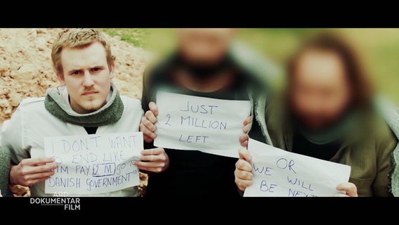 Drei Personen knien auf dem Boden und halten Zettel mir Forderungen auf Englisch in die Kamera. "Just 2 Million left". Von zwei Personen sind die Gesichter geblurrt. © Screenshot 