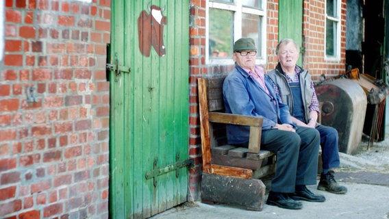 Zwei ältere Herren sitzen auf einer Bank.  