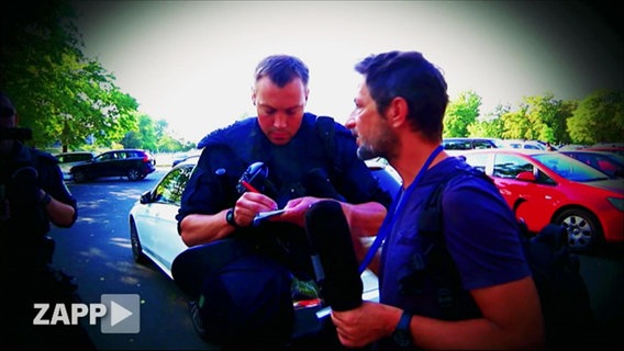 Polizist nimmt Personalien von Kameramann auf  