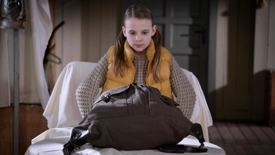 Szene aus Die Pfefferkörner Folge 186: Ein kleines Mädchen schaut sich einen großen Rucksack an.  
