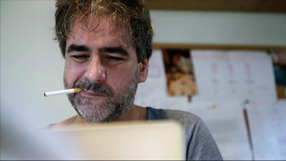 Deniz Yücel sitzt vor seinem Computer, eine Zigarette im Mundwinkel.  