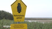 Ein gelbes Schild mit einer Eule darauf, das das Naturschutzgebiet Kronenloch / Speicherkoog Dithmarschen auszeichnet.  