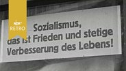 Schild in einem Schaufenster mit der Aufschrift "Sozialismus, das ist Frieden und stetige Verbesserung des Lebens!"  