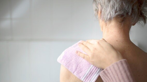 Bildausschnitt zeigt die nackte Nacken-Schulter-Partie einer älteren Frau mit grauen Haaren von hinten. Darauf der Arm einer anderen Person, die ihr mit einem Waschlappen über die Schulter reibt. © picture alliance / photothek Foto: Ute Grabowsky