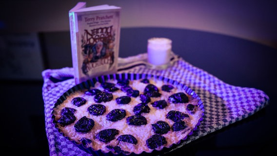 Ein Kuchen und ein Buch sind auf einem Küchentuch arrangiert. © NDR/ Tim Piotraschke Foto: Tim Piotraschke