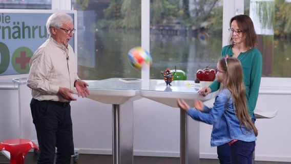 Doc Jörn Klasen wirft einem kleinen Mädchen einen Ball zu, die Mutter schaut zu. © NDR Foto: Moritz Schwarz, Oliver Zydek