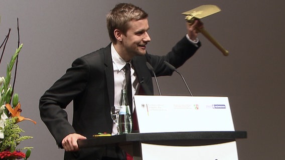 Tobias Schlegl hält einen goldenen Klappspaten hoch. © NDR Foto: Screenshot