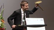 Tobias Schlegl hält einen goldenen Klappspaten hoch. © NDR Foto: Screenshot