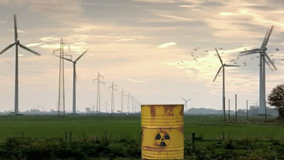 Ein Atommüllfass steht vor einer langen Reihe Windräder. © NDR Foto: Screenshot