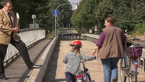 Ein Mann im Anzug und zwei Passanten auf einer Brücke  