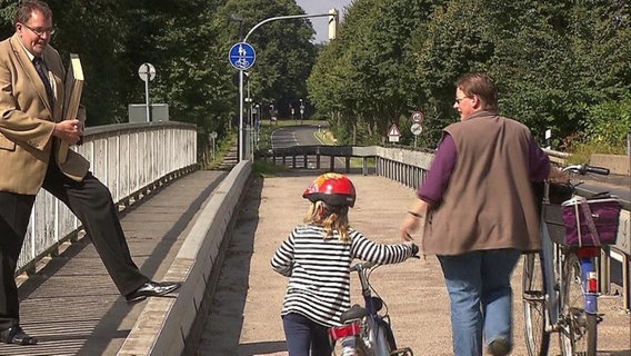 Ein Mann im Anzug und zwei Passanten auf einer Brücke  